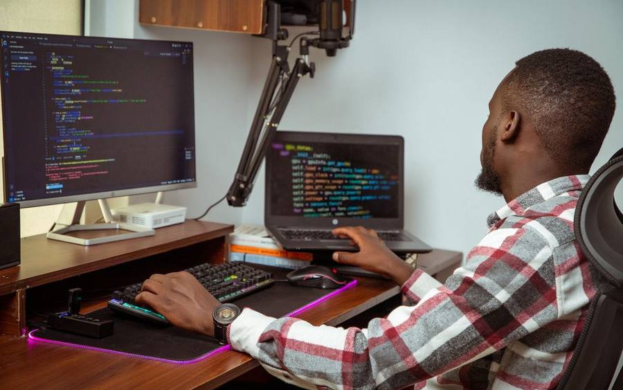 Un développeur au travail devant deux écrans, du code affiché.